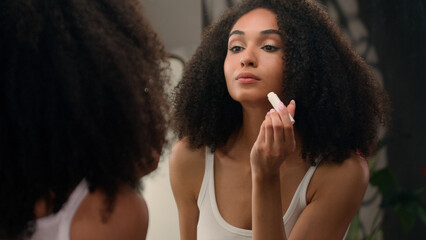 Beautiful African American woman looking in mirror reflection morning beauty routine preparation...