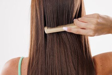Young woman brushing her long brown straight hair on white background, back view
