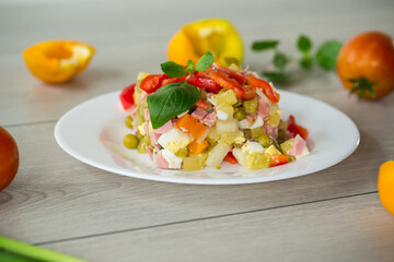 vegetable salad of boiled vegetables, with peas, sausage, sweet pepper. On a wooden table