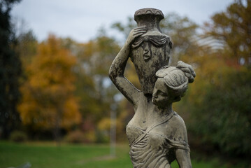 Fototapeta premium In autumn, the park transforms into a breathtaking scene as leaves turn golden, red, and orange, blanketing the ground in warm colors while a crisp breeze stirs the air.