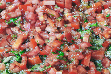 A close up of a bowl of chopped tomatoes and herbs. The tomatoes are red and the herbs are green. The bowl is filled with a variety of tomatoes and herbs, creating a colorful and appetizing dish