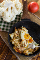 fried omelette with cauliflower and vegetables in a frying pan on a wooden table