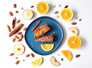 Creative layout made of carrot cake  with cinnamon sticks and oranges with lemon on the plate on the white background. Flat lay. Food concept. Macro concept. 