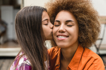Mixed-race interracial mother and daughter spending time together outdoors, kissing bonding on a...