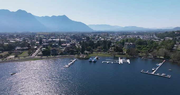 Zoom out aerial shot of the La Poza viewpoint in the city of Pucon, Chile. Boats on the water and mountains in the background adorn the landscape