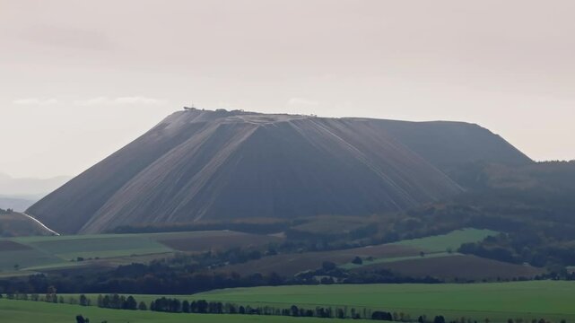 Drone video of Monte Kali in Heringen, Germany, showcasing the striking white salt mound against the surrounding landscape. Drone move right.
