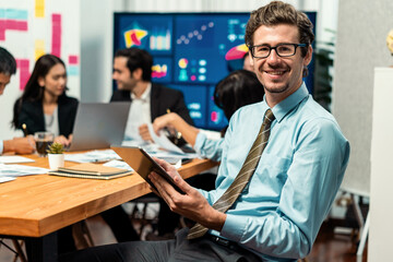 Portrait of businessman or analyst looking at camera with his colleague analyzing data analysis in dynamic business strategy investment planning meeting. Meticulous