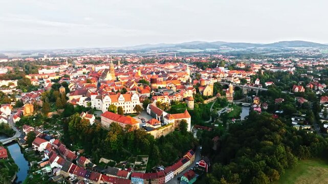 Drone wide-angle shot of Bautzen at sunset, capturing the historic cityscape bathed in warm, fading light. The scene highlights the town's iconic architecture and scenic skyline. Drone move left.