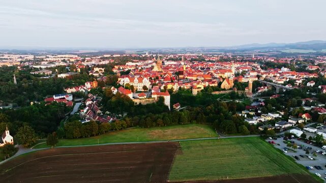 Drone wide-angle shot of Bautzen at sunset, capturing the historic cityscape bathed in warm, fading light. The scene highlights the town's iconic architecture and scenic skyline. Drone move left.