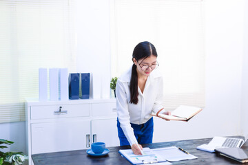 An Asian woman sits at her desk, surrounded by files  , embodying dedication and professionalism in her work.