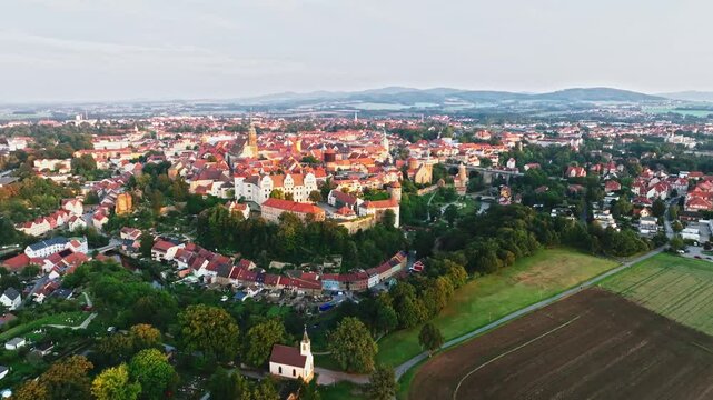 Drone wide-angle shot of Bautzen at sunset, capturing the historic cityscape bathed in warm, fading light. The scene highlights the town's iconic architecture and scenic skyline. Drone move right.