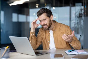 Mature businessman experiencing stress during work, overwhelmed by tasks, using laptop in modern...