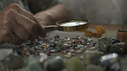 Elderly woman examining polished stones through magnifying glass. Close-up.