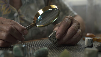 Elderly woman examining polished stones through magnifying glass. Close-up.