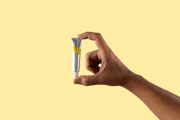 Male hand holding a yellow paint tube isolated on yellow background