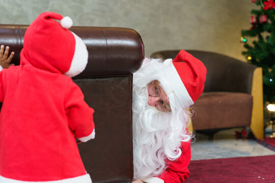 Santa Claus playing hide and seek with baby in red costume