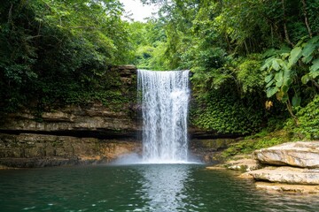 Obraz premium Scenic waterfall surrounded by lush green forest in a tranquil setting.