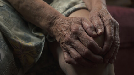 Fototapeta premium Elderly woman massaging her knee while sitting on sofa. Hand close-up. 