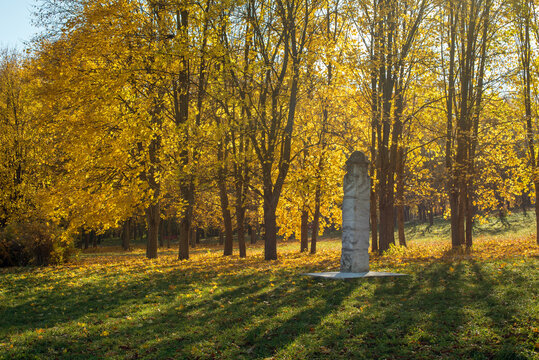 The park in autumn is filled with bright yellow leaves, stands a majestic idol sculpture made of stone, this stone sculpture is full of symbolism and depth