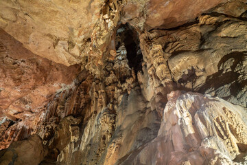 A cave with a lot of rock formations and a small opening. Scene is mysterious and eerie.