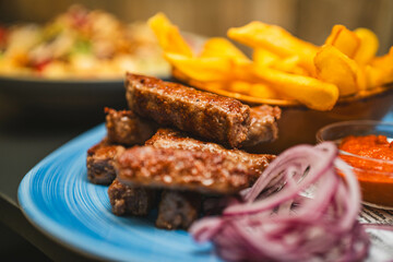 Juicy BBQ ribs served with crispy fries and red onions on a blue plate. Ideal for restaurant menus, food blogs, or social media, showcasing a classic comfort food dish.