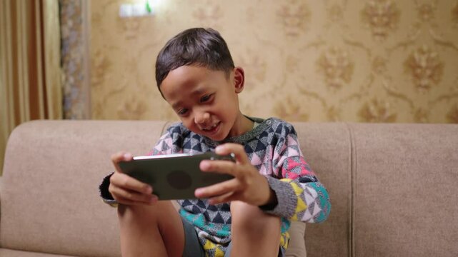 A happy child plays an online game on his smartphone, showing intense focus and excitement. The expression expresses love for virtual games