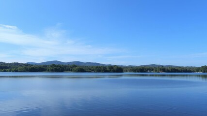 A serene landscape of a peaceful lake reflecting the surrounding greenery and sky, water surface, outdoors
