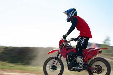 Motocross racing. A motorcyclist wearing protective clothing and a helmet rides a motorcycle standing up at high speed. A boy rides a motorcycle off-road.
