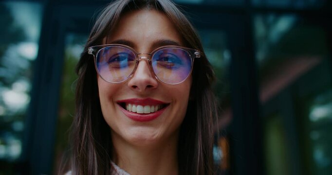 Attractive Caucasian woman looking at sky before glancing at camera and smiling. Wearing big round glasses for better vision. Portrait concept. Manager spending time outside during lunch break.