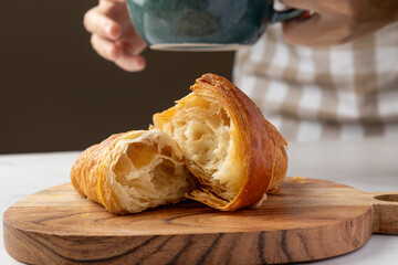 A beautifully flaky croissant is halved on a wooden board with a rustic teal mug in the background, showcasing a cozy and delicious morning breakfast scene.