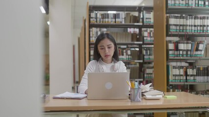 Asian female student research in library and using laptop preparing for exam