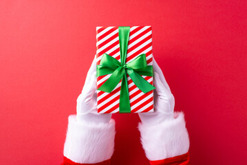 Santa Claus in traditional costume holding a bright red and white striped gift with a green ribbon...
