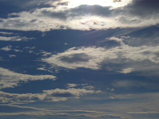 Blue sky with sun behind clouds and sunlight - natural background. Topics: sun energy, weather, meteorology, atmosphere, air space