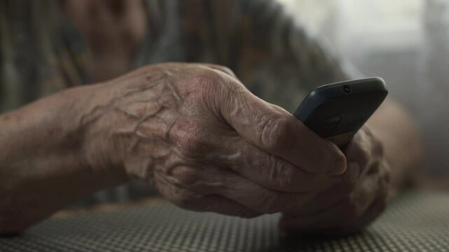 Elderly woman dialing number on push-button mobile phone. Hands close-up.