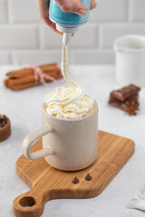 Woman hand squeezes whipped cream into cup with cocoa