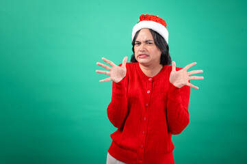 An Asian woman in a red sweater and Santa hat, with a green background, makes a disgusted face with her hands spread out in front of her, as if recoiling. She displays a humorous