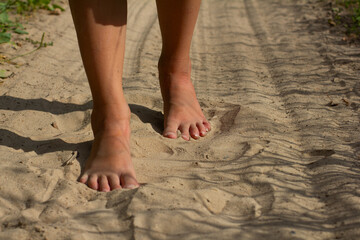 Fototapeta na wymiar A child happily walks barefoot along a sandy path in the countryside on a sunny summer day, enjoying the beauty and freedom of nature. A barefoot child walks on soft, warm sand in the summer.