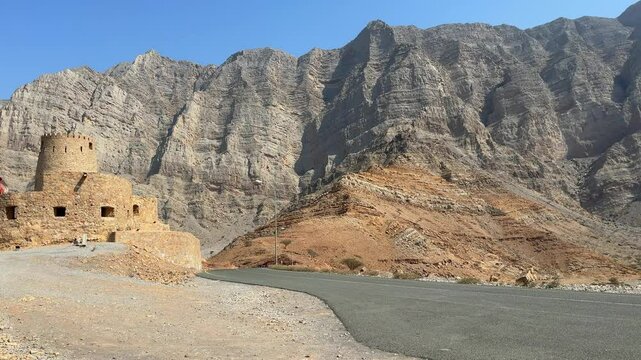 historic stone fort in Bukha, Musandam, Oman, against the backdrop of mountains, with the Omani flag waving from the tower Al Qalaa Fort