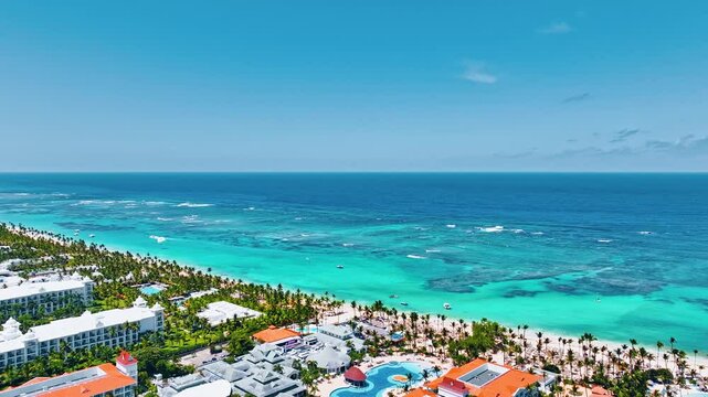 Aerial view of tropical resort beach on Caribbean coast in Dominican Republic. Ocean on sunny summer day, aerial view. Beautiful tropical beach with palm trees, umbrellas and parasailing balloon.