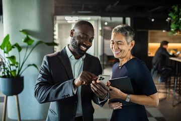 Business colleagues smiling and looking at smartphone in modern office
