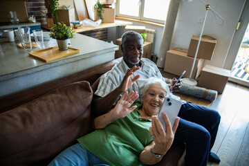 Senior couple relaxing on couch with smartphones after moving in