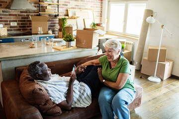 Senior couple relaxing on couch with smartphones after moving in