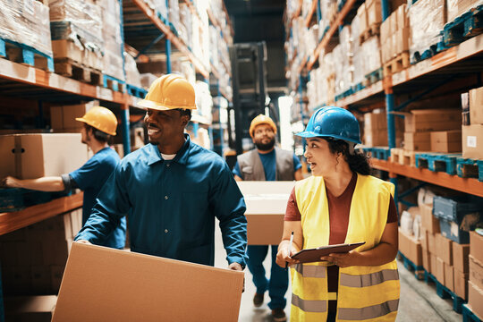 Warehouse workers in hard hats checking inventory and lifting boxes