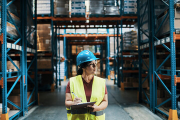 Warehouse supervisor inspecting inventory with clipboard and yellow hard hat