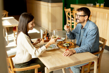 Couple enjoying a romantic dinner together in a cozy restaurant, celebrating with a toast over delicious cuisine on a warm evening