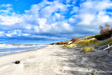 a sand dune with a beach in the background and a blue cloudy sky 