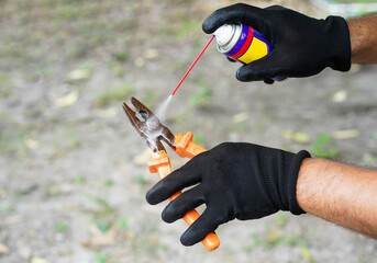 Man hands with black glove use lubricating oil spray to an old steel pliers prepare before work or...