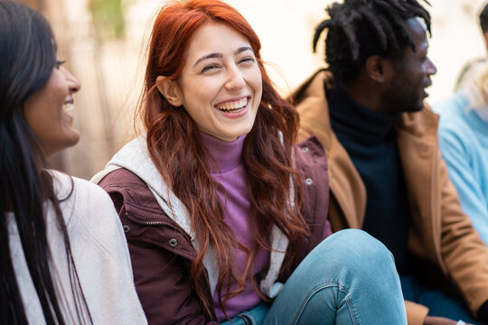 Multicultural friends sharing laughter outdoors in natural winter light - Candid portrait of diverse casual young people hangout enjoying social time together