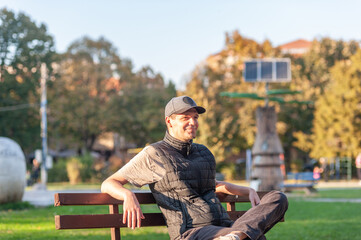 A cheerful man is sitting alone in the park on the bench and enjoying the autumn sun	