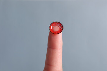 Woman holding color contact lens on light grey background, closeup